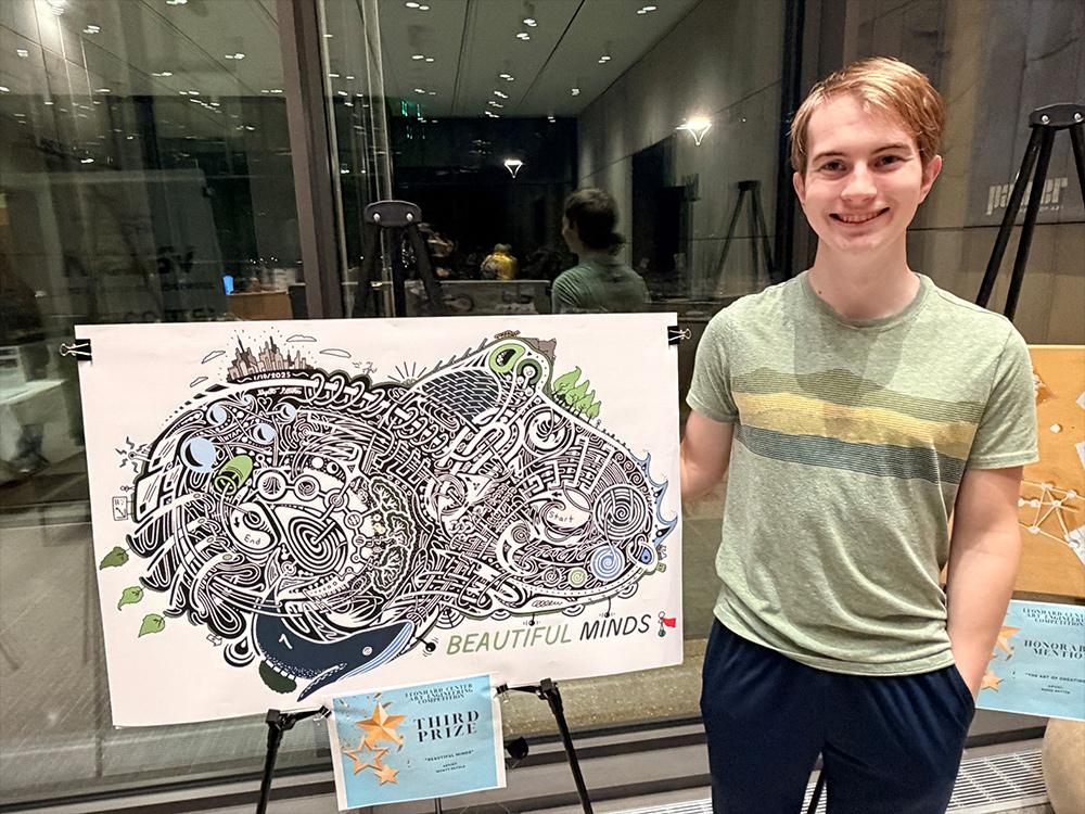 A photo of Wyatt Petula standing beside his artwork, a primarily black-and-white, intricate maze featuring a series of images which include a whale, various greenery, a city skyline, solar panels, water and more. 