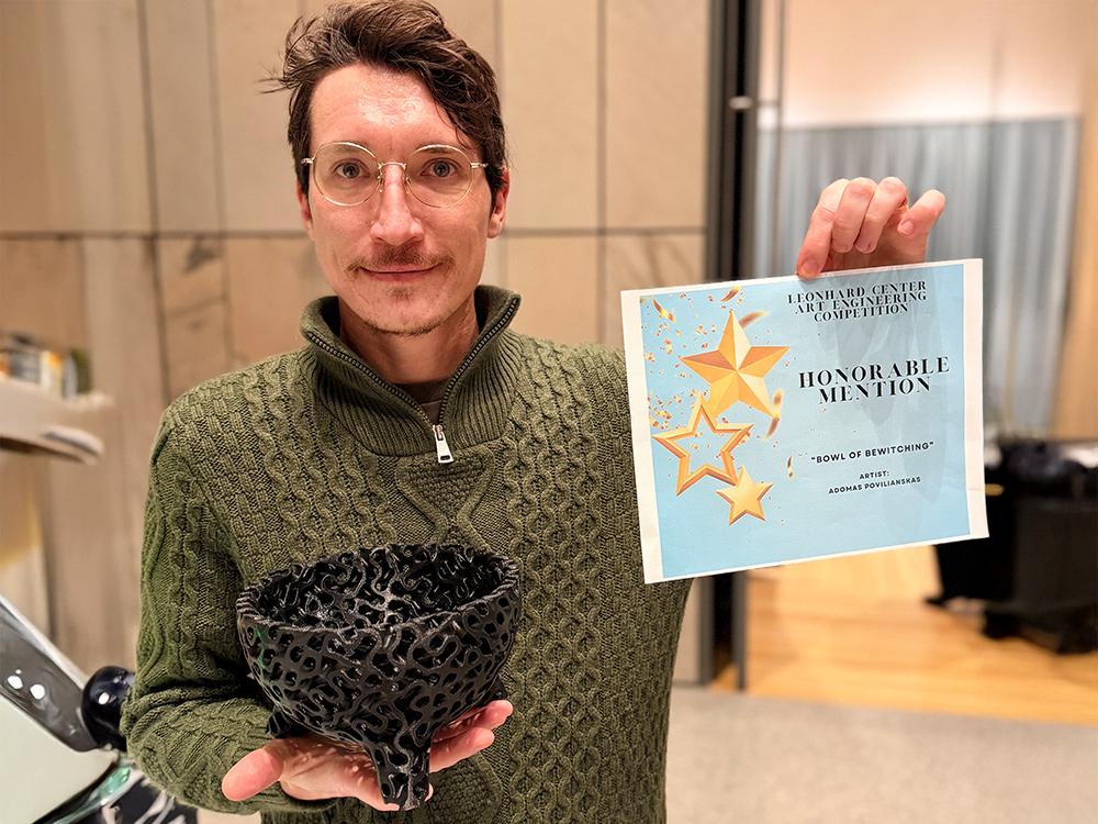A photo of Adomas Povilianskas holding an honorable mention award in one hand and a black bowl in the other.  