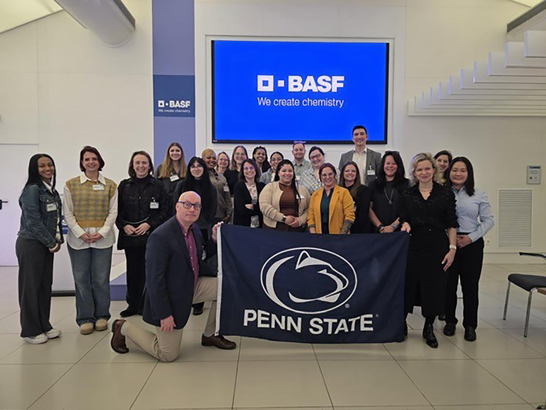 A group of people holding a navy Penn State flag in a conference room.