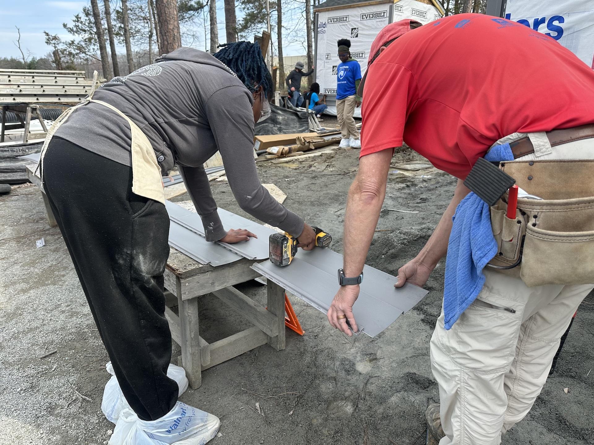 student and volunteer cutting a piece of siding for a house