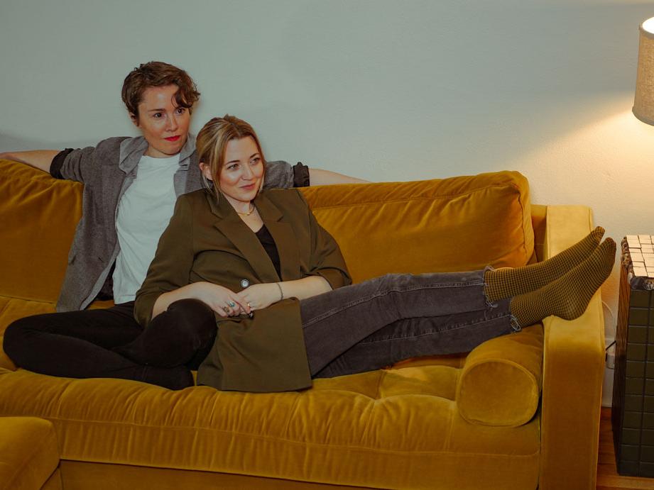 Two women recline on a couch.