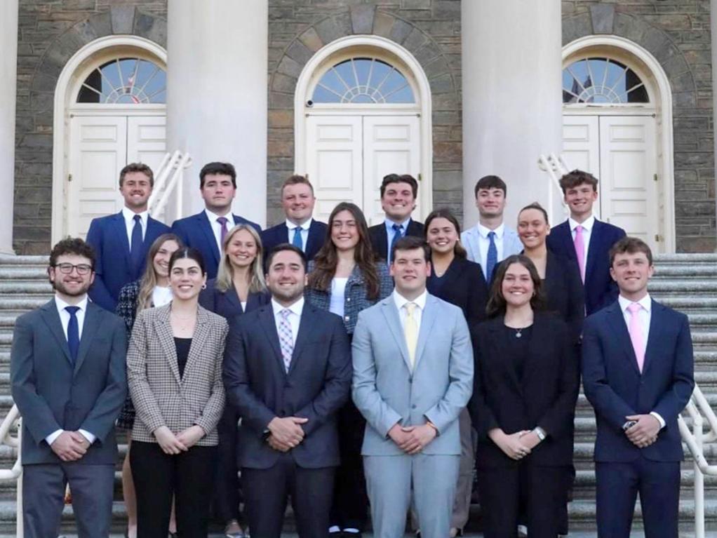 Jessica Amatrudo wears a plaid blazer and white top while standing with other students in front of Old Main Building.