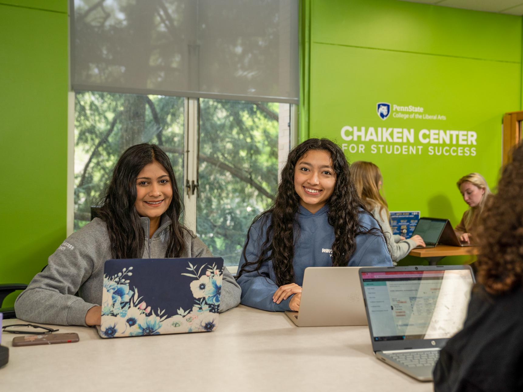 Two students smiling at the camera, inside the Liberal Arts Chaiken Center.