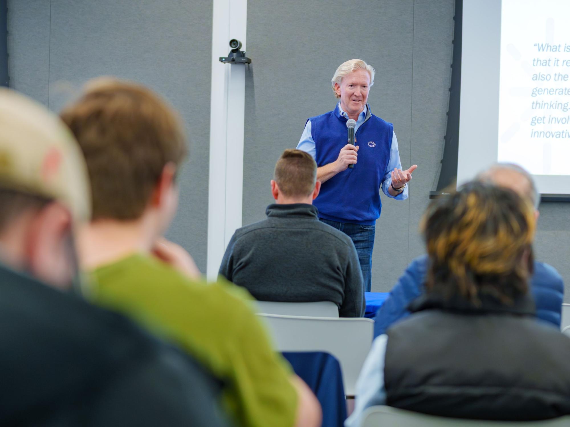 person holding microphone speaks to audience in classroom