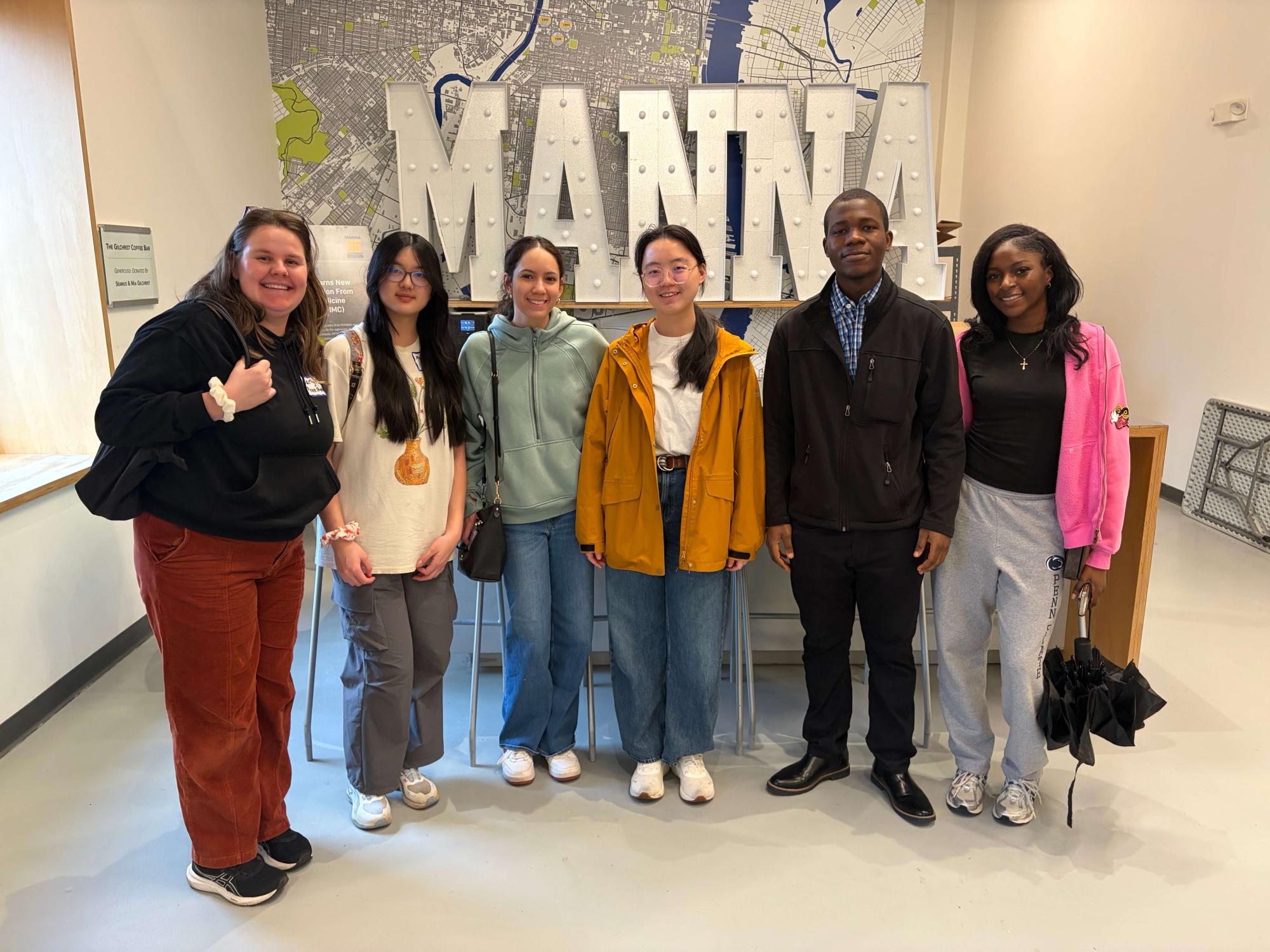 Six people standing in front of a white sign that reads MANNA.
