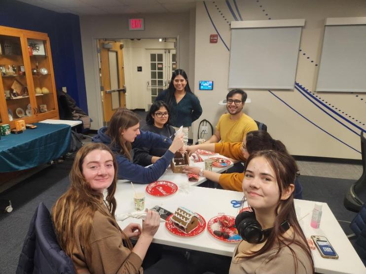 A group of students smile while assembling gingerbread houses.