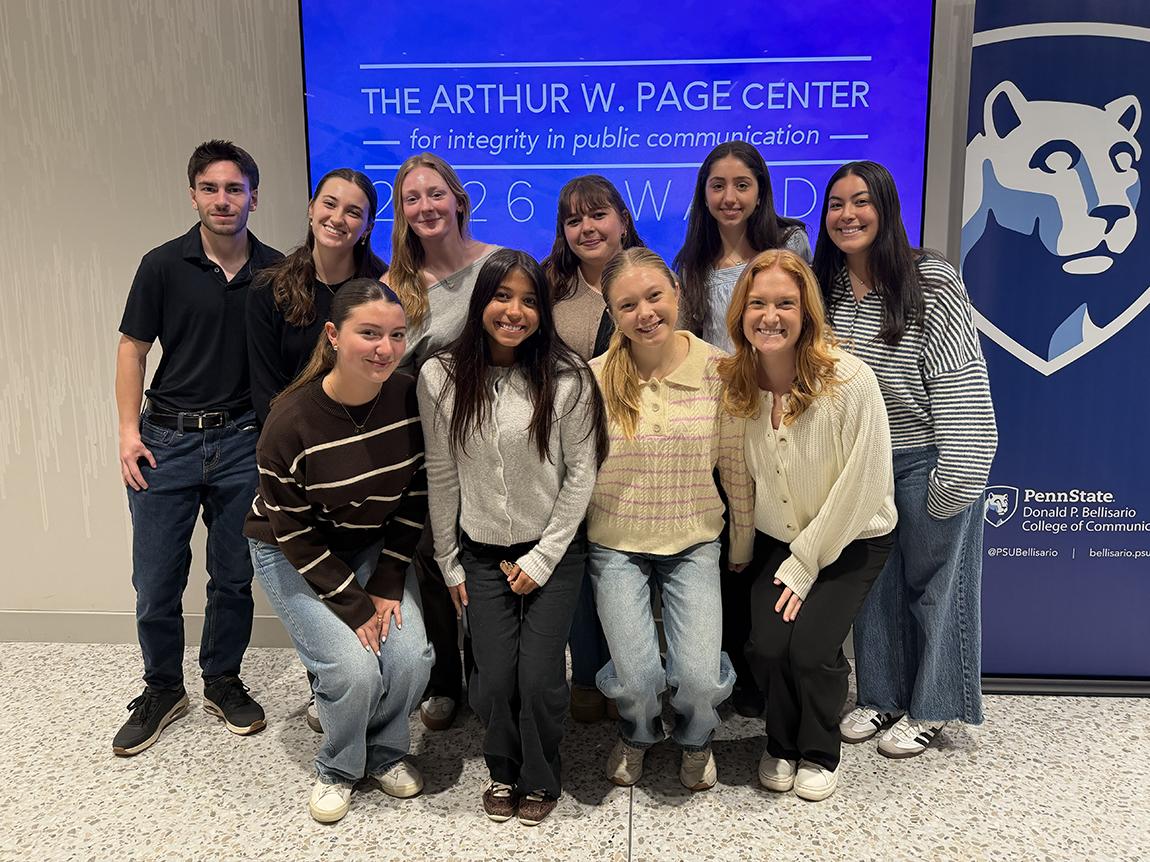 Students stand in front of a screen and banner.
