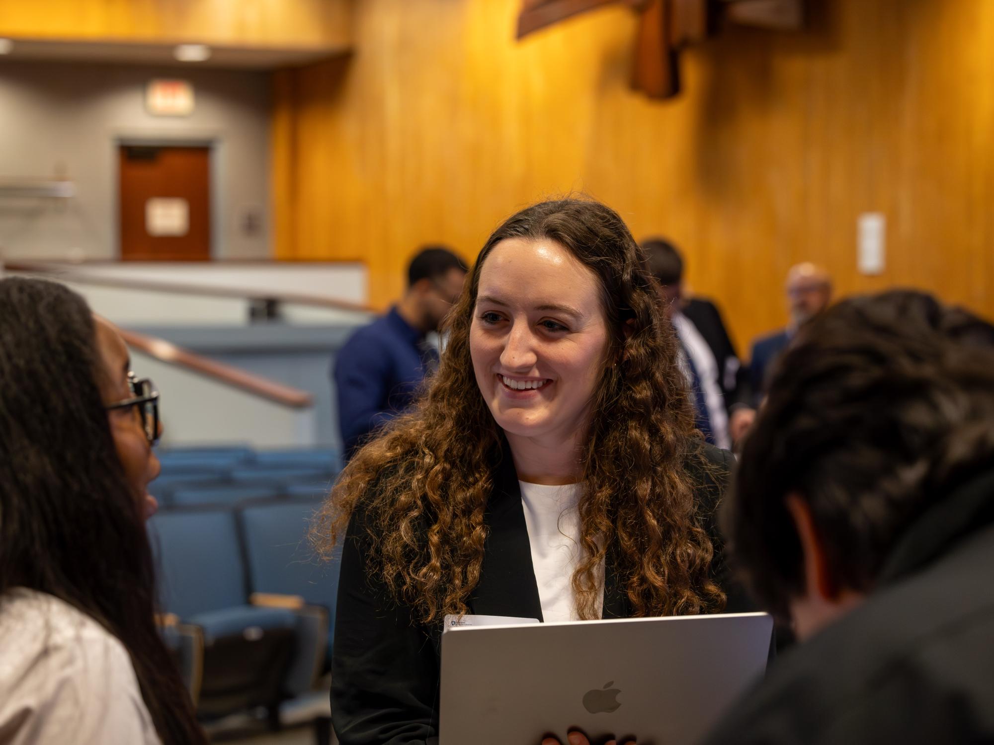 Sophia Mrazik wears a blazer and smiles while holding a laptop
