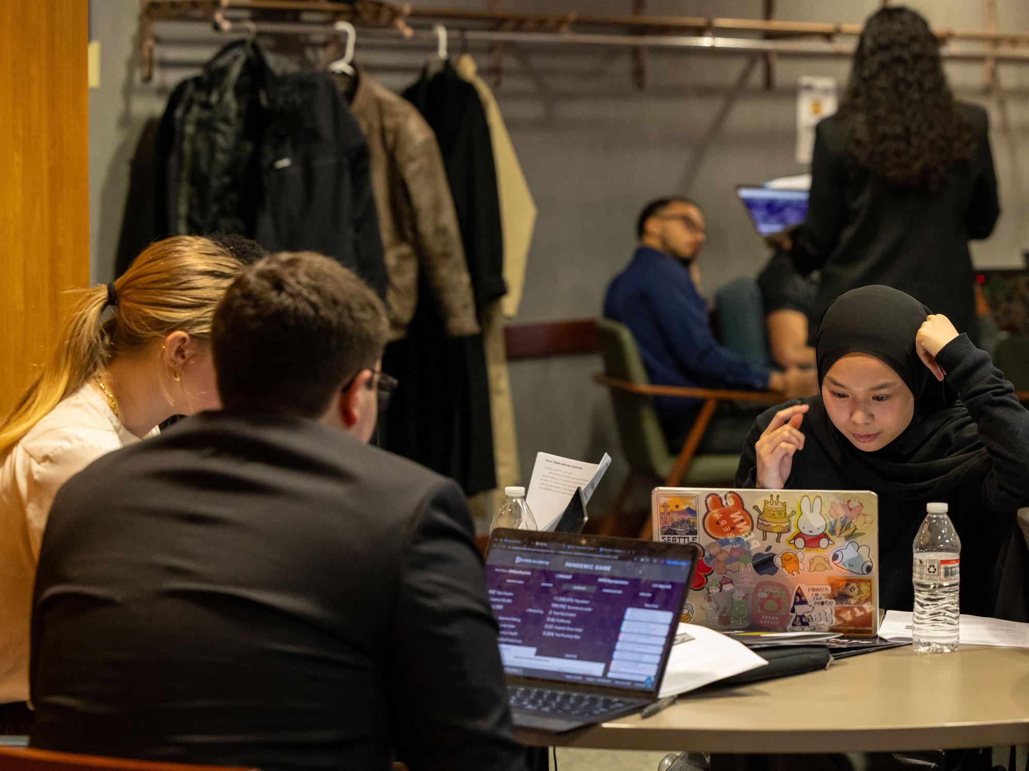 Three students sit around a table while working on laptops