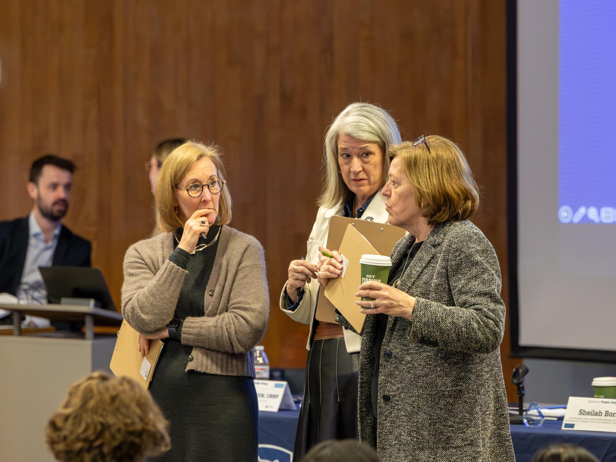 Three women with clipboards discuss teams during the simulation.