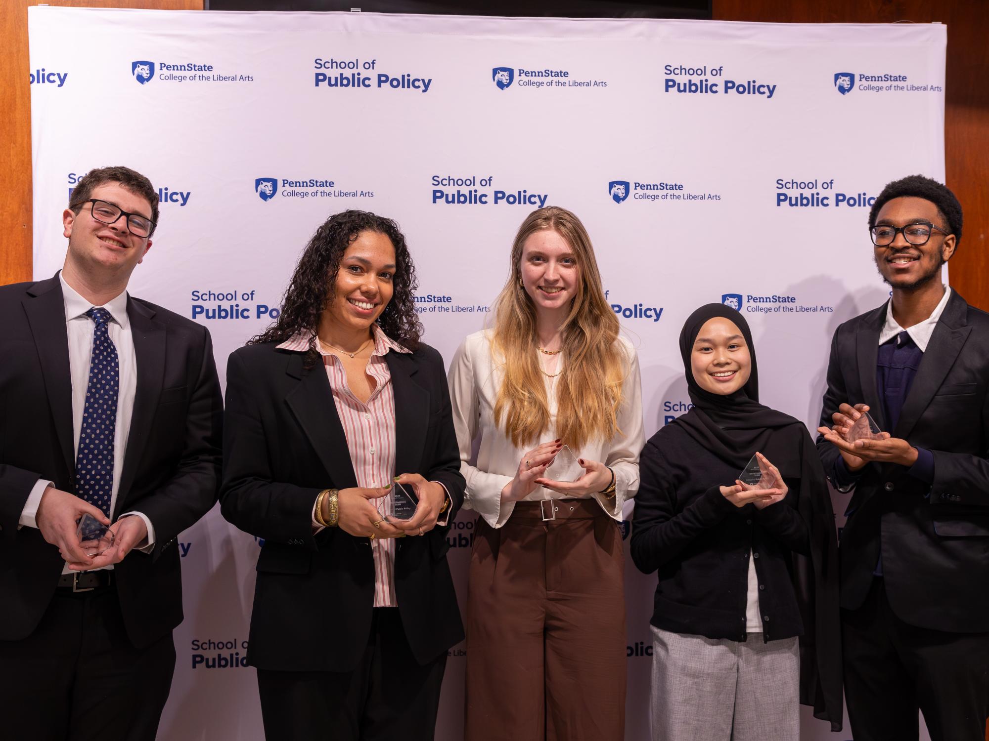The winning team poses with their awards in front of a School of Public Policy banner.