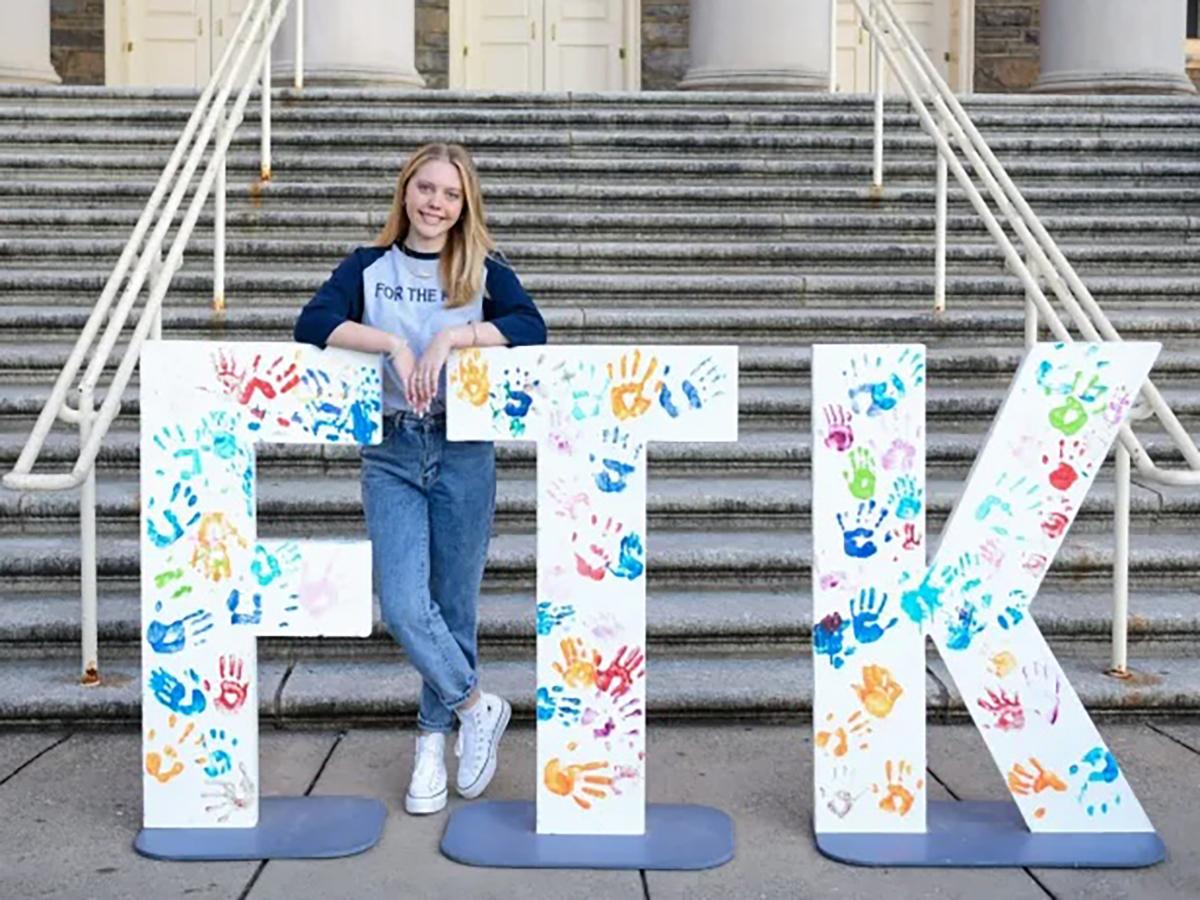 Kristen Donahoe leans on the letters F and T of FTK in front of the Old Main steps