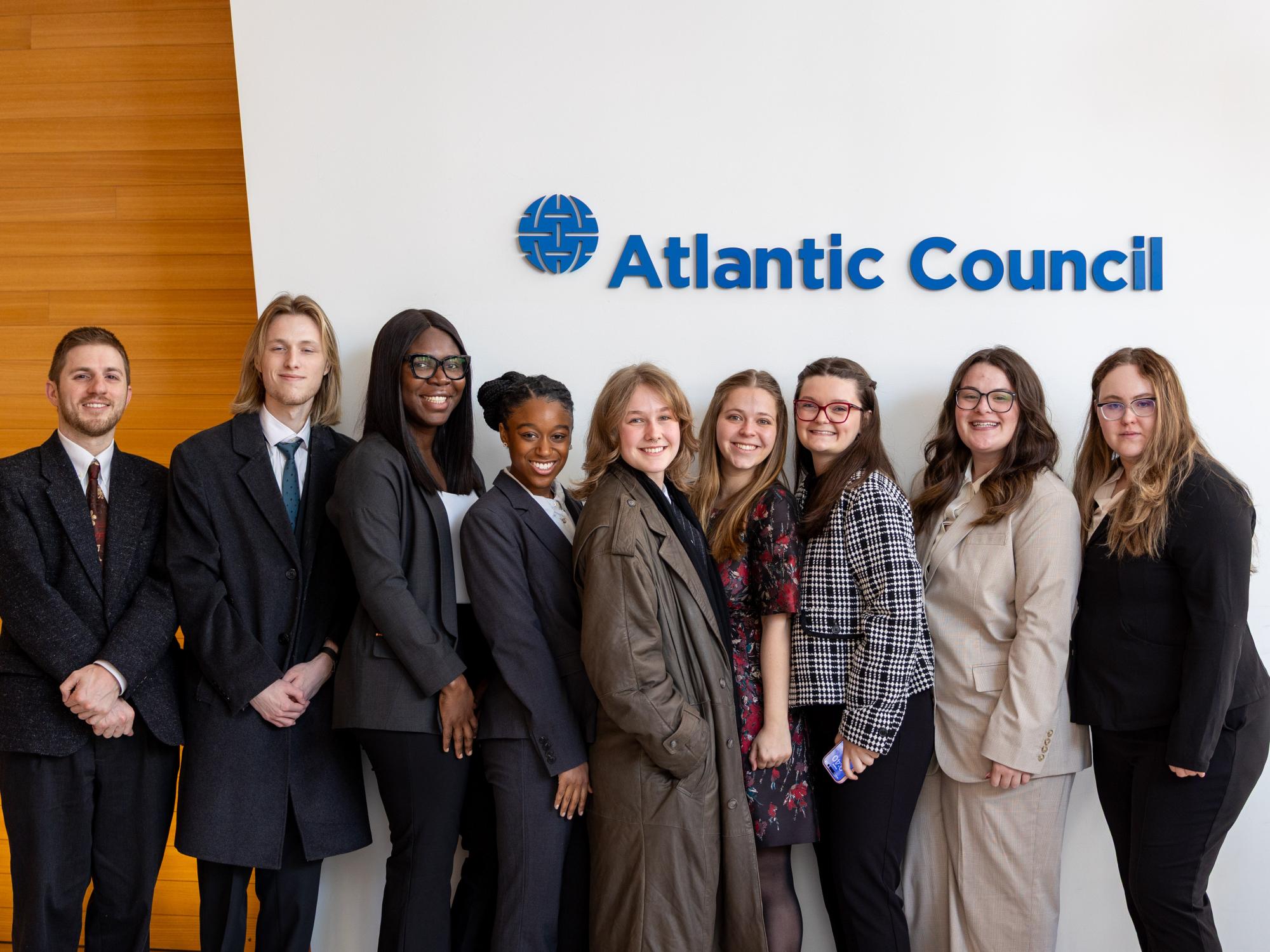A group of students stand in front of an Atlantic Council sign. 