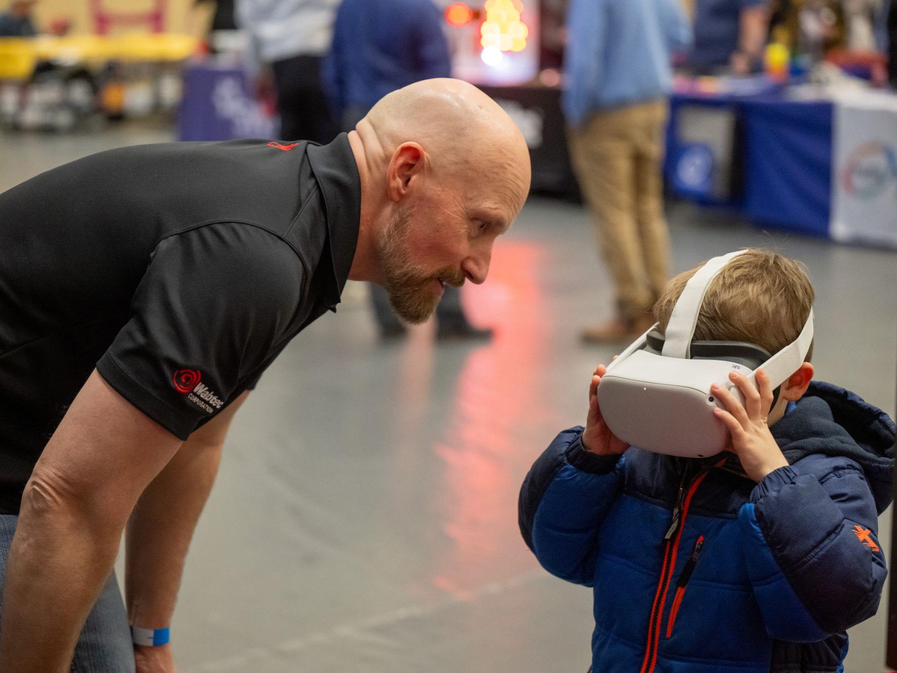 A man leans down toward a child who is wearing a virtual-reality headset