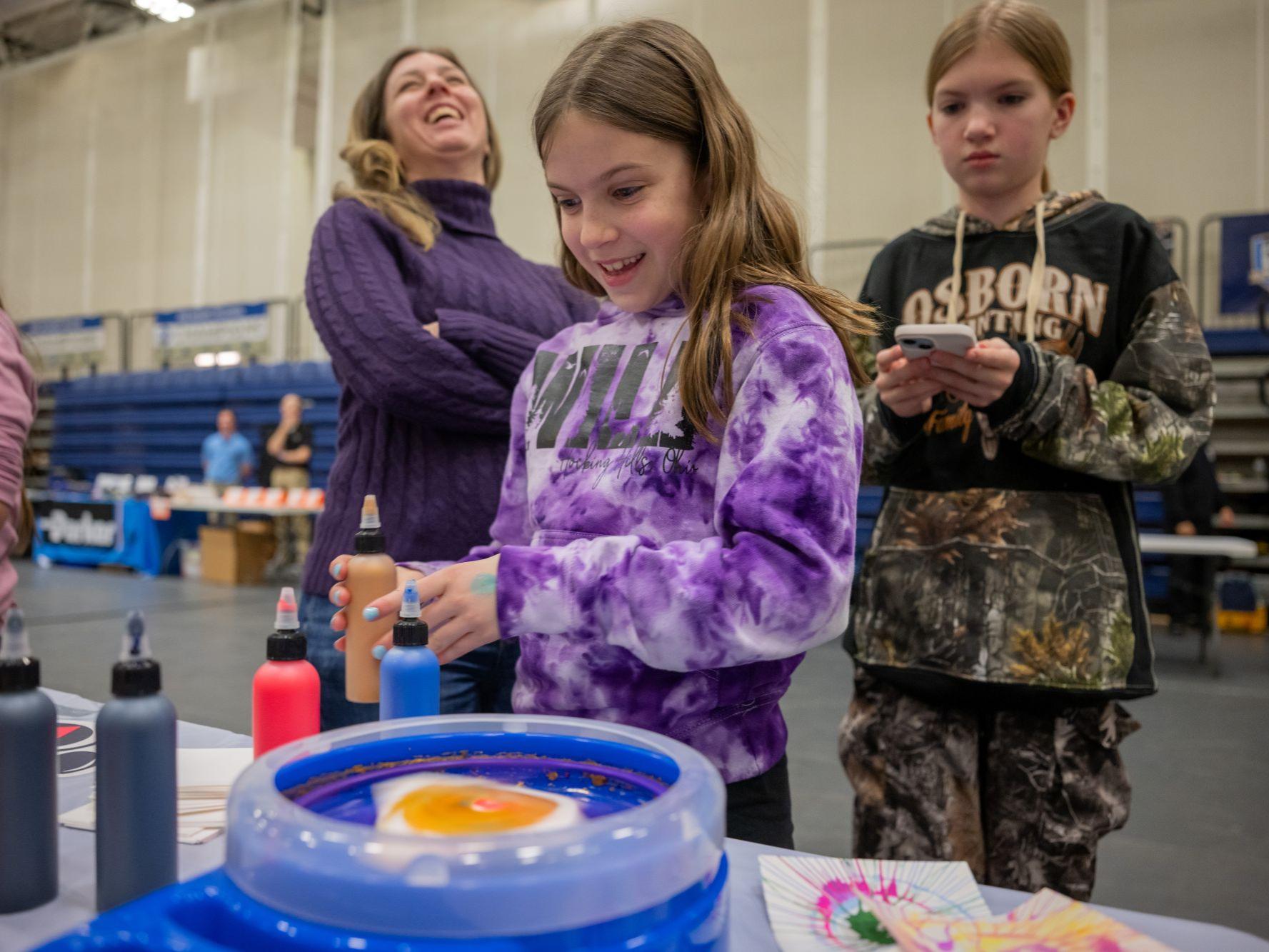 A girl and her mother laugh at a spin-art activity station at Penn State Behrend's STEAM Fair.