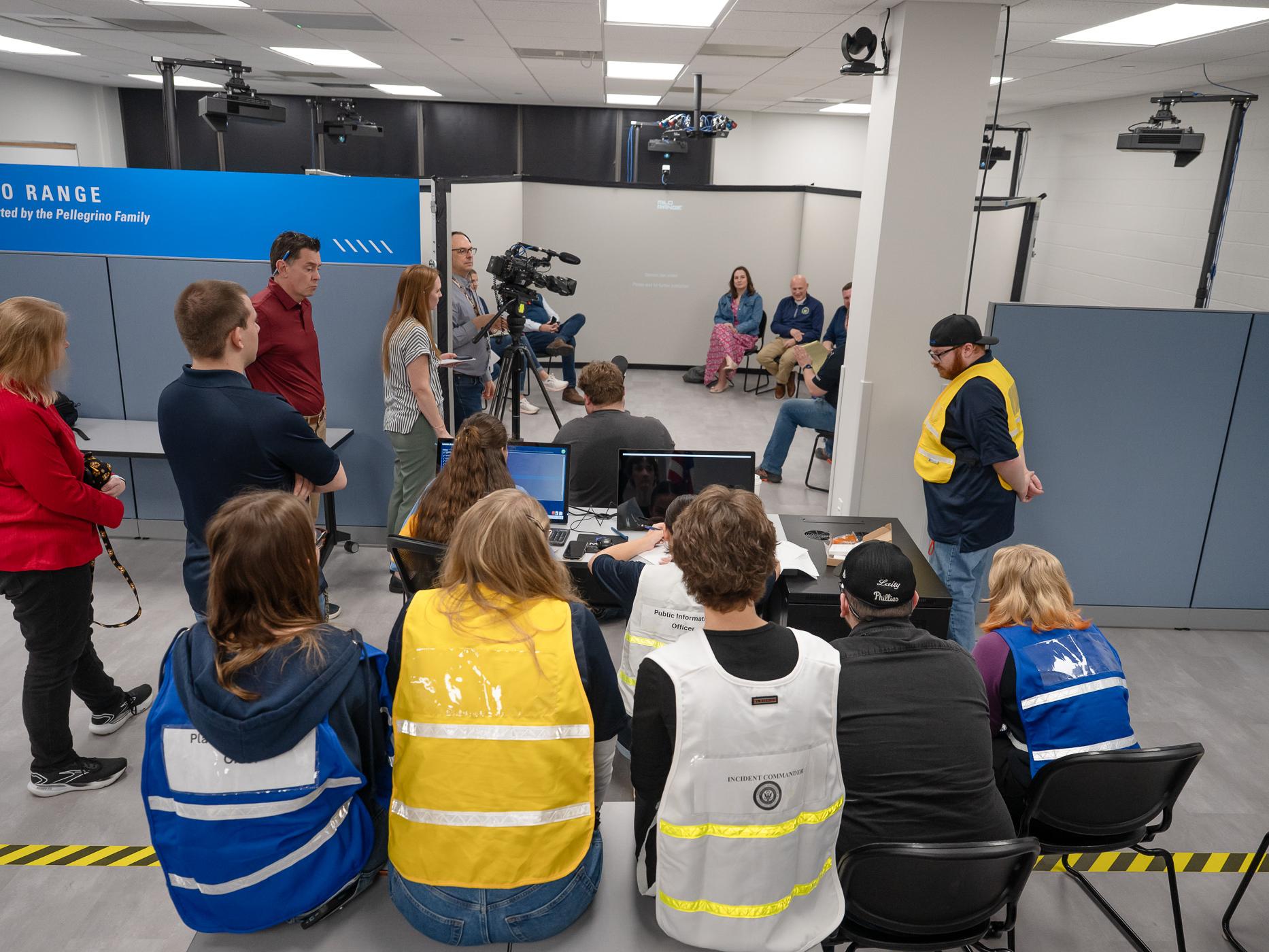 A group of people gather round each other for a mock press conference with cameras