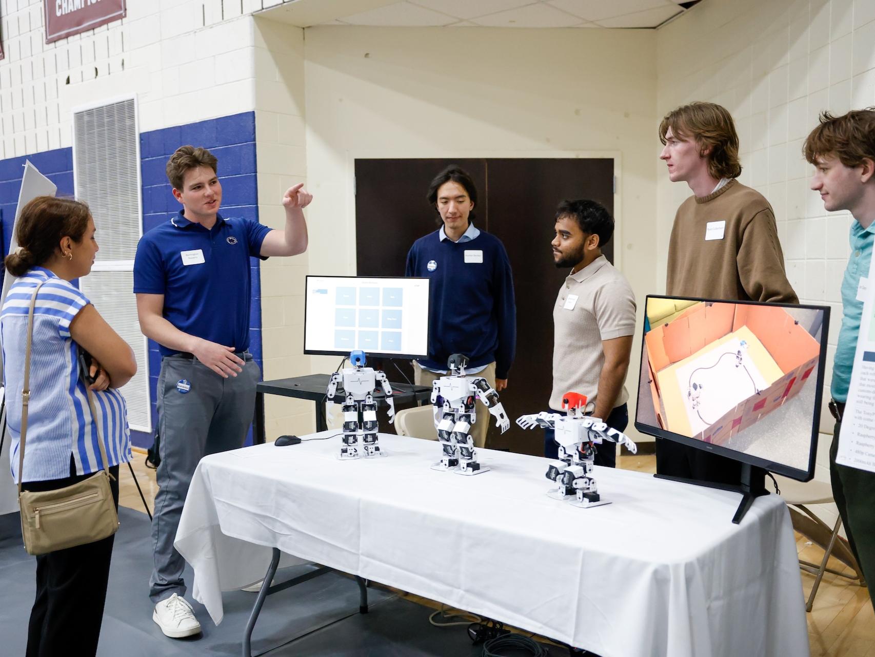 vie students talking to professor about project with robots and tv screens