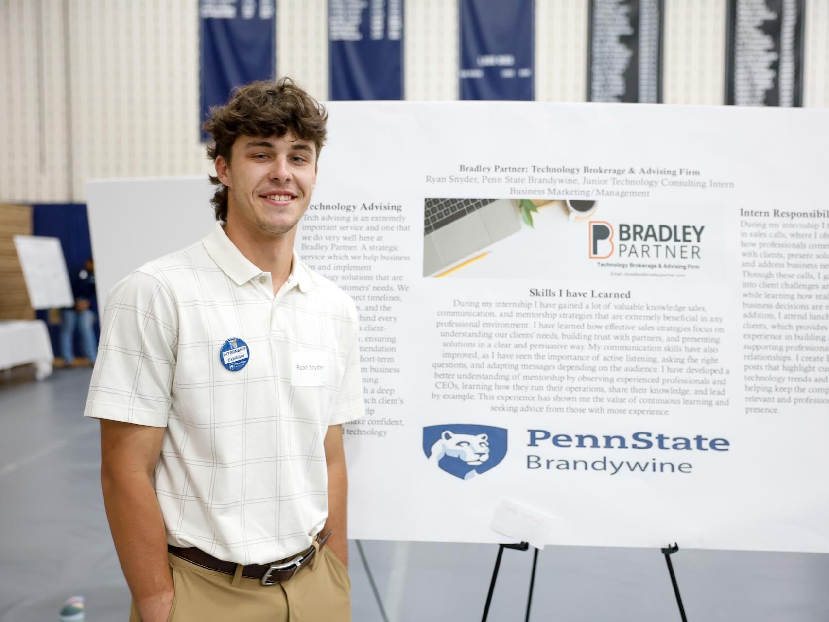 student standing in front of poster about his business internship at Bradley Partner