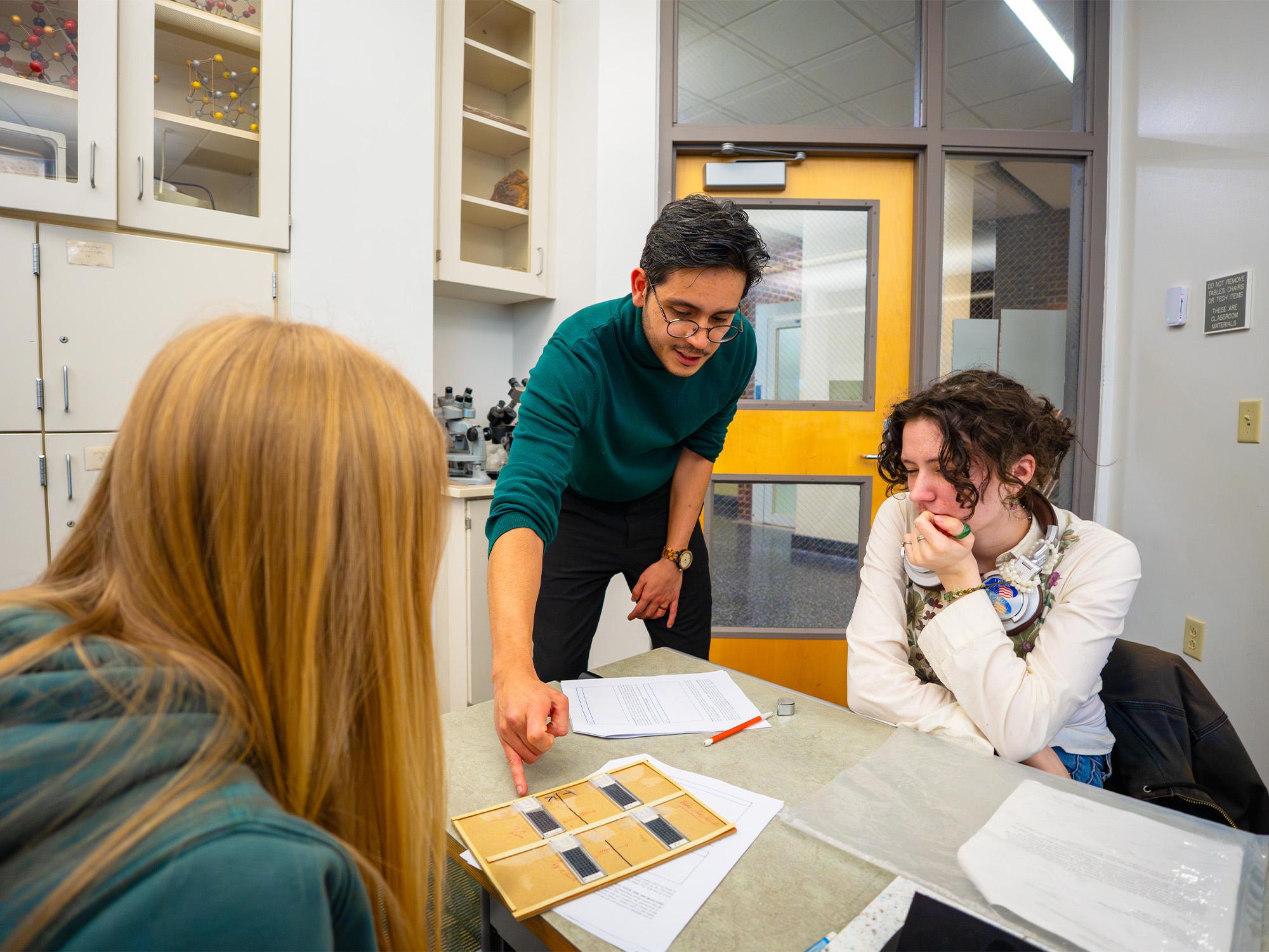 male instructor points to geology sample on desk in front of two students