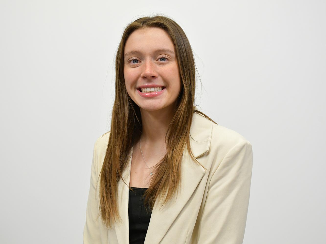 A young woman with long hair wearing a white blazer and black shirt