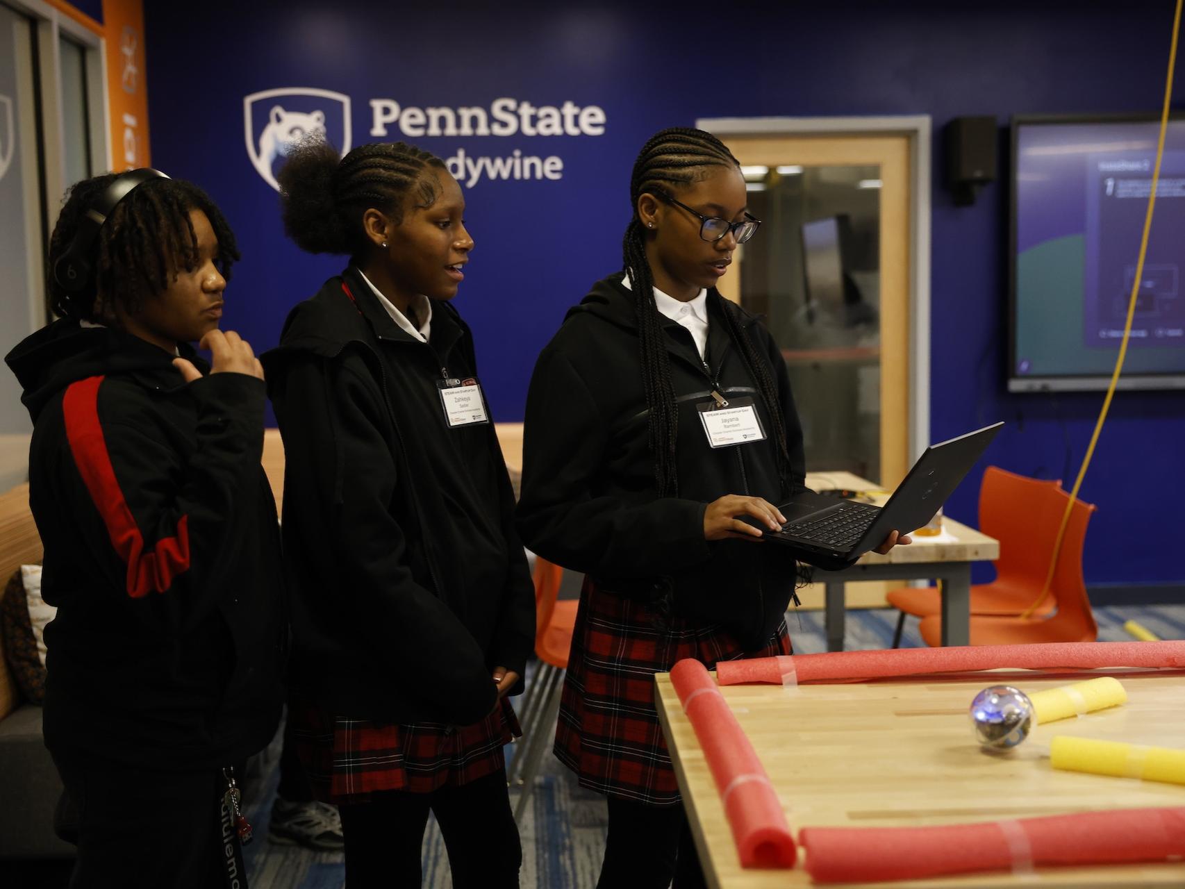 three students with laptop moving a ball on a tabletop