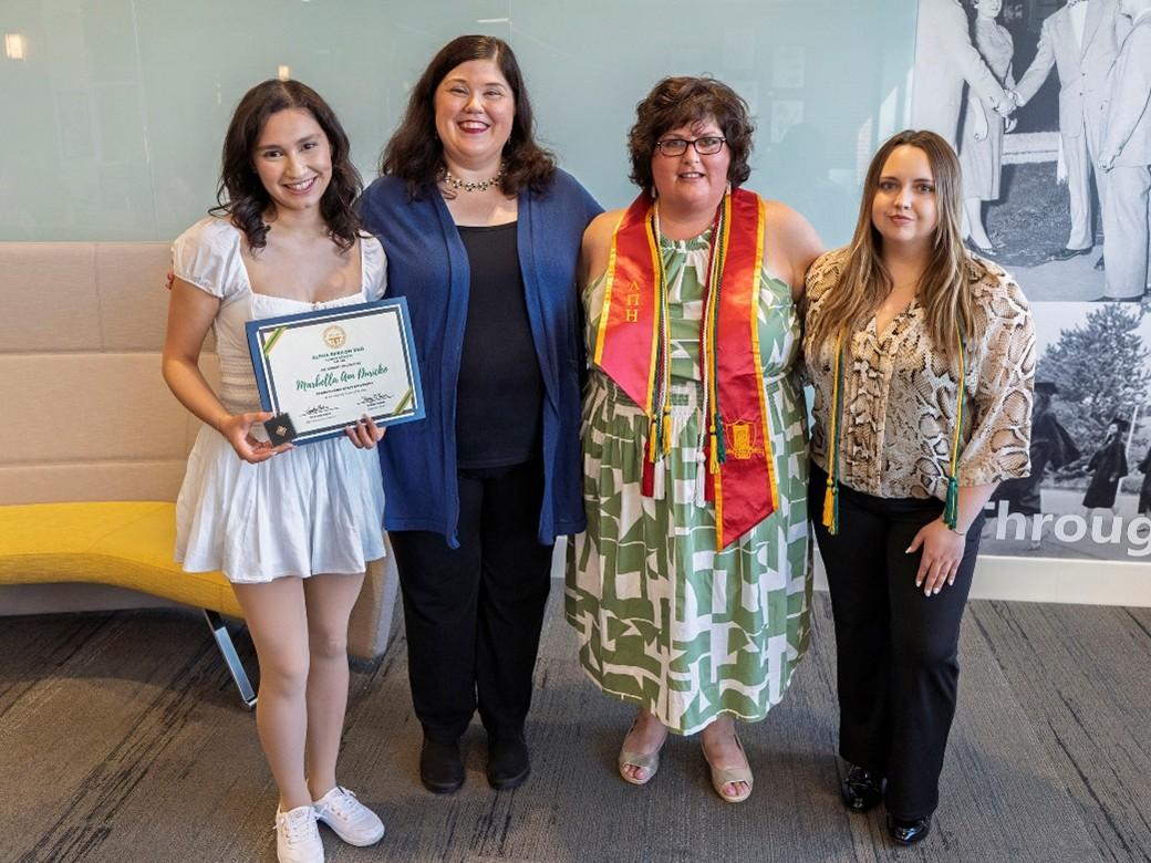 Communications professor Stephanie Longo, second from left poses for a photo with three of her students wearing their cords and one holding an award certificate