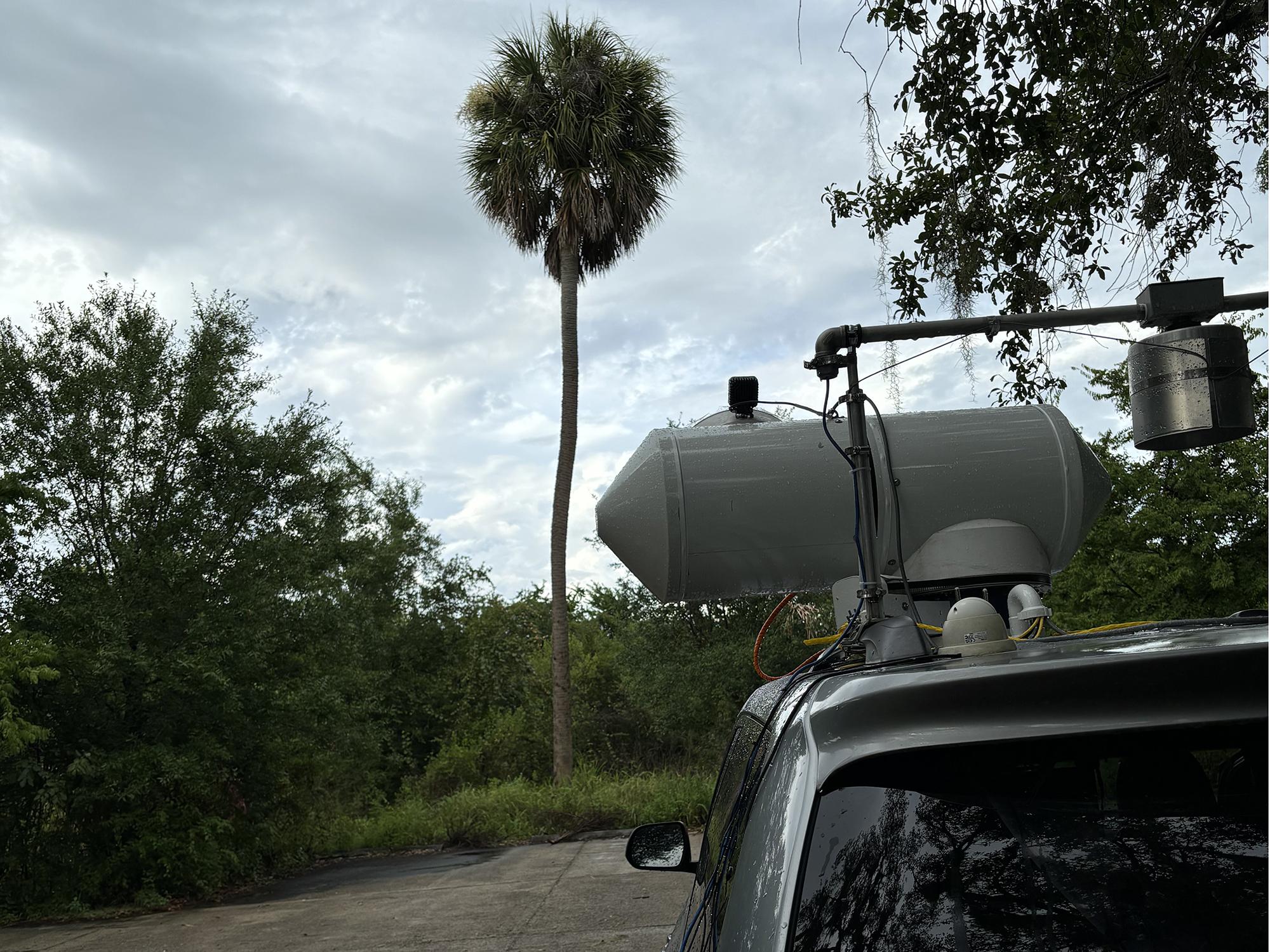 The periscope on top of a Toyota Sienna research van pointed at a Palm Tree under a thunderstorm