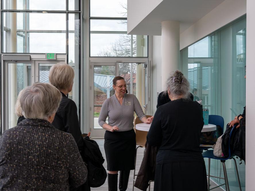 A woman stands at a table while she addresses a group of people.