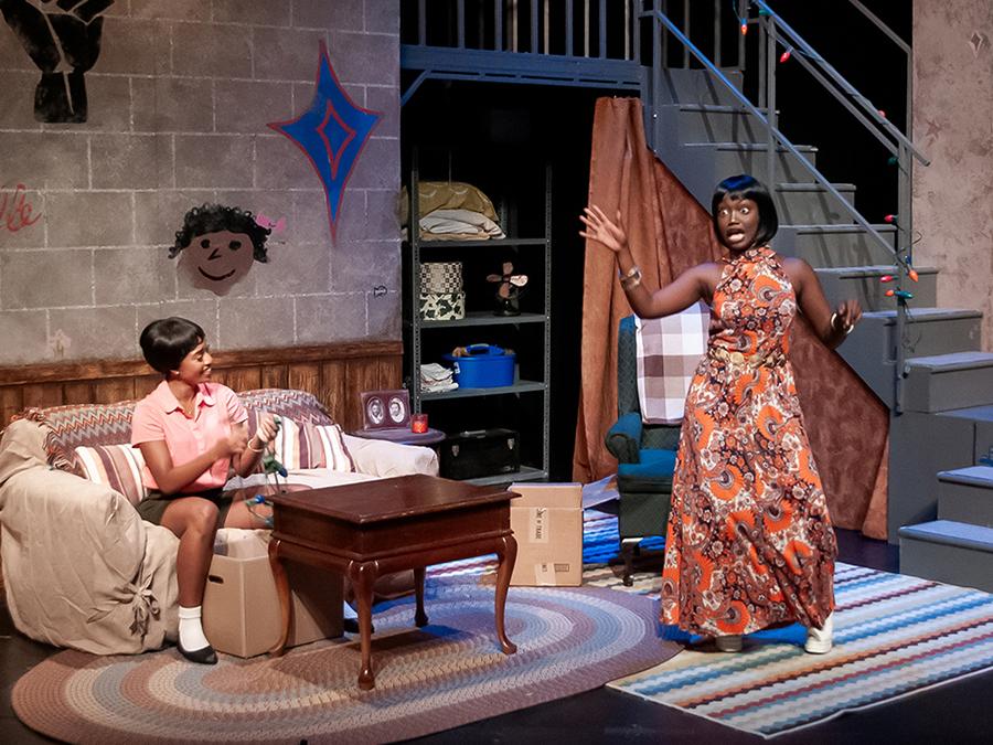 Two actors on a stage made to look like an apartment in the 1960s