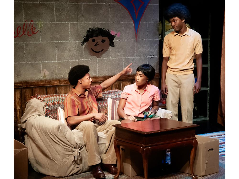 Three actors talk to each other on a stage made to look like an apartment in the 1960s