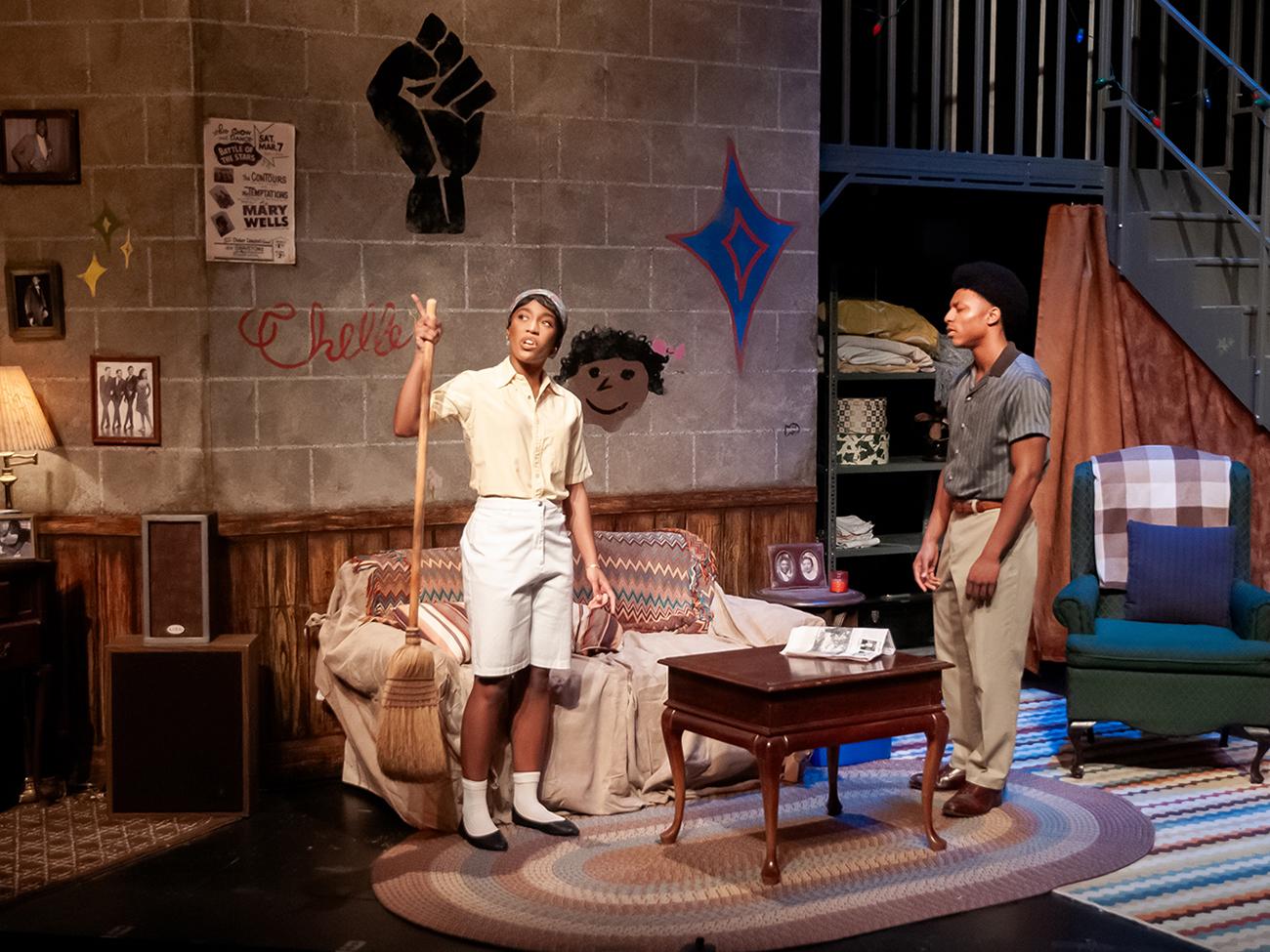 Two actors on a stage made to look like an apartment in the 1960s