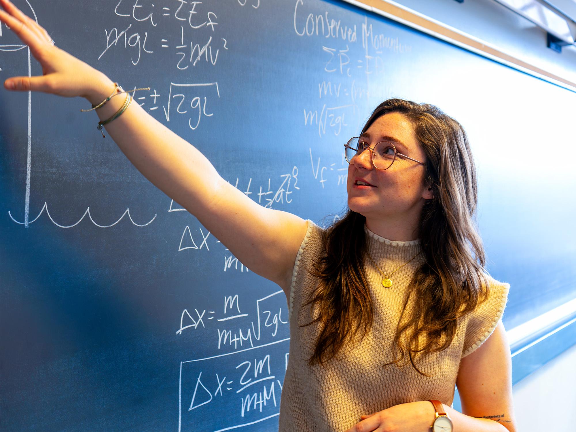 female points to writing on chalkboard