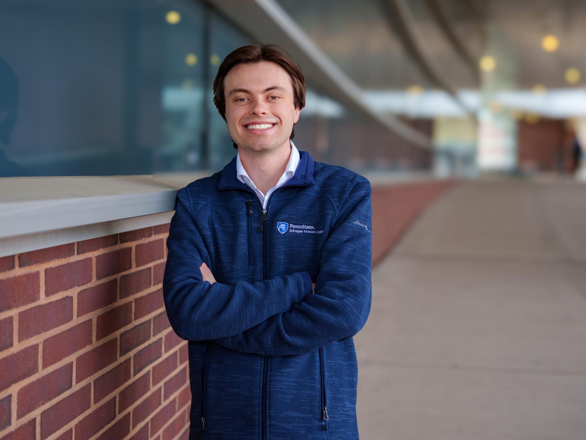 person with arms crossed leans against brick and glass building