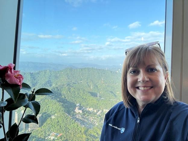 A woman smiling in front of a window, which shows a stunning view of mountains