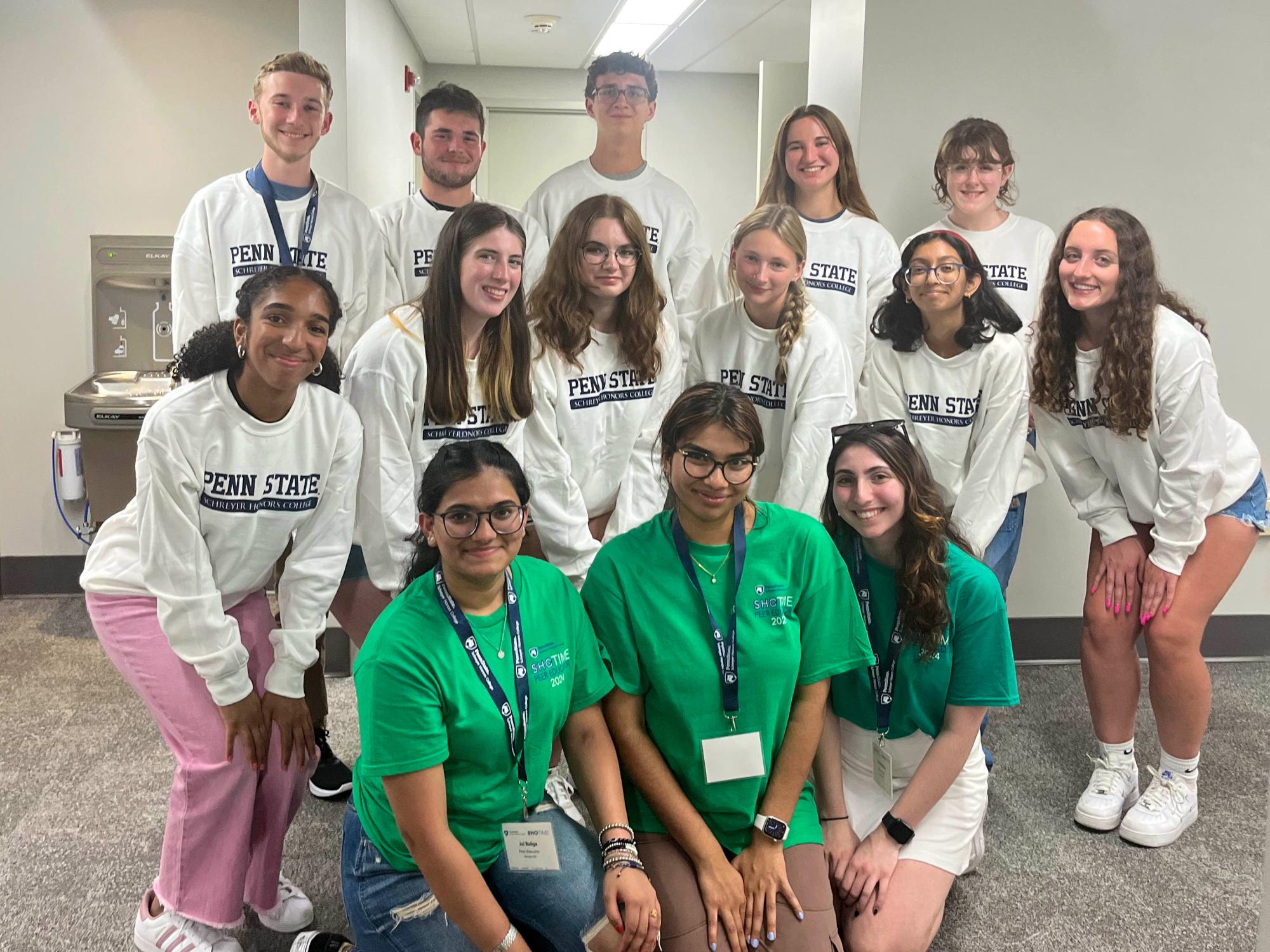 Jui Baliga poses with people indoors at Penn State, with the back row in white “PENN STATE” shirts and the front row in green shirts with lanyards.