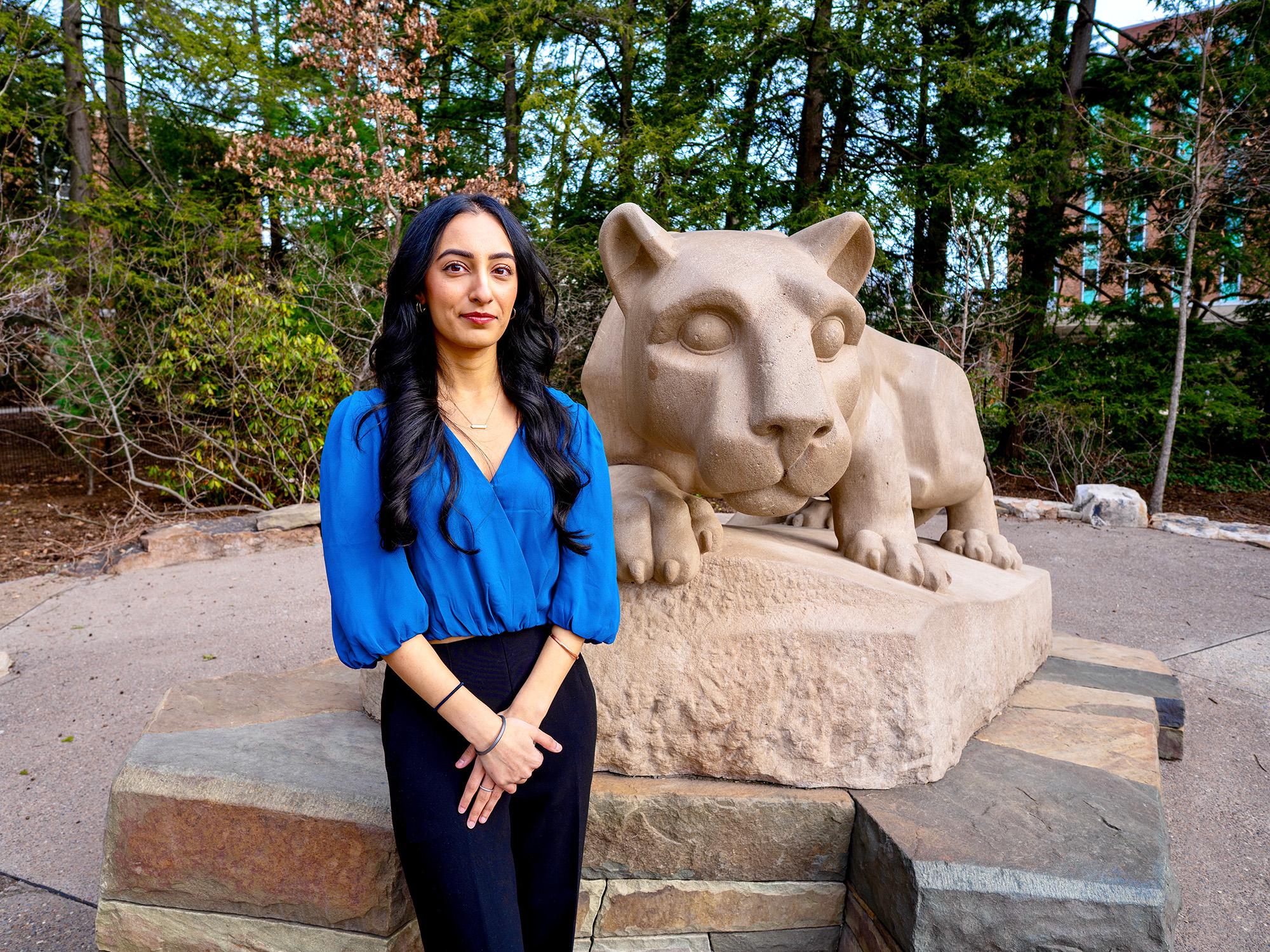 woman in blue blouse standing next to Nittany Lion statue