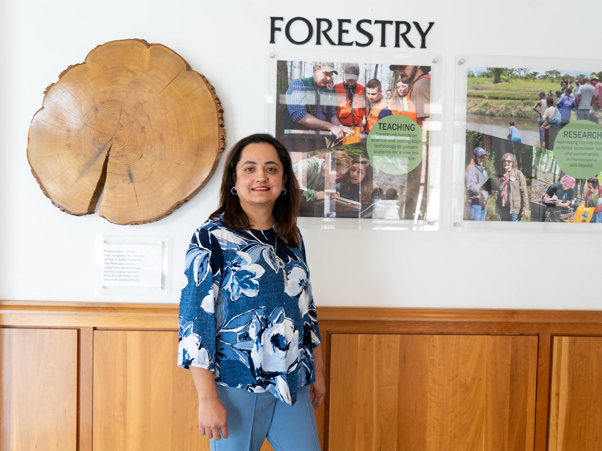 woman stands in front of cross section of tree and forestry sign