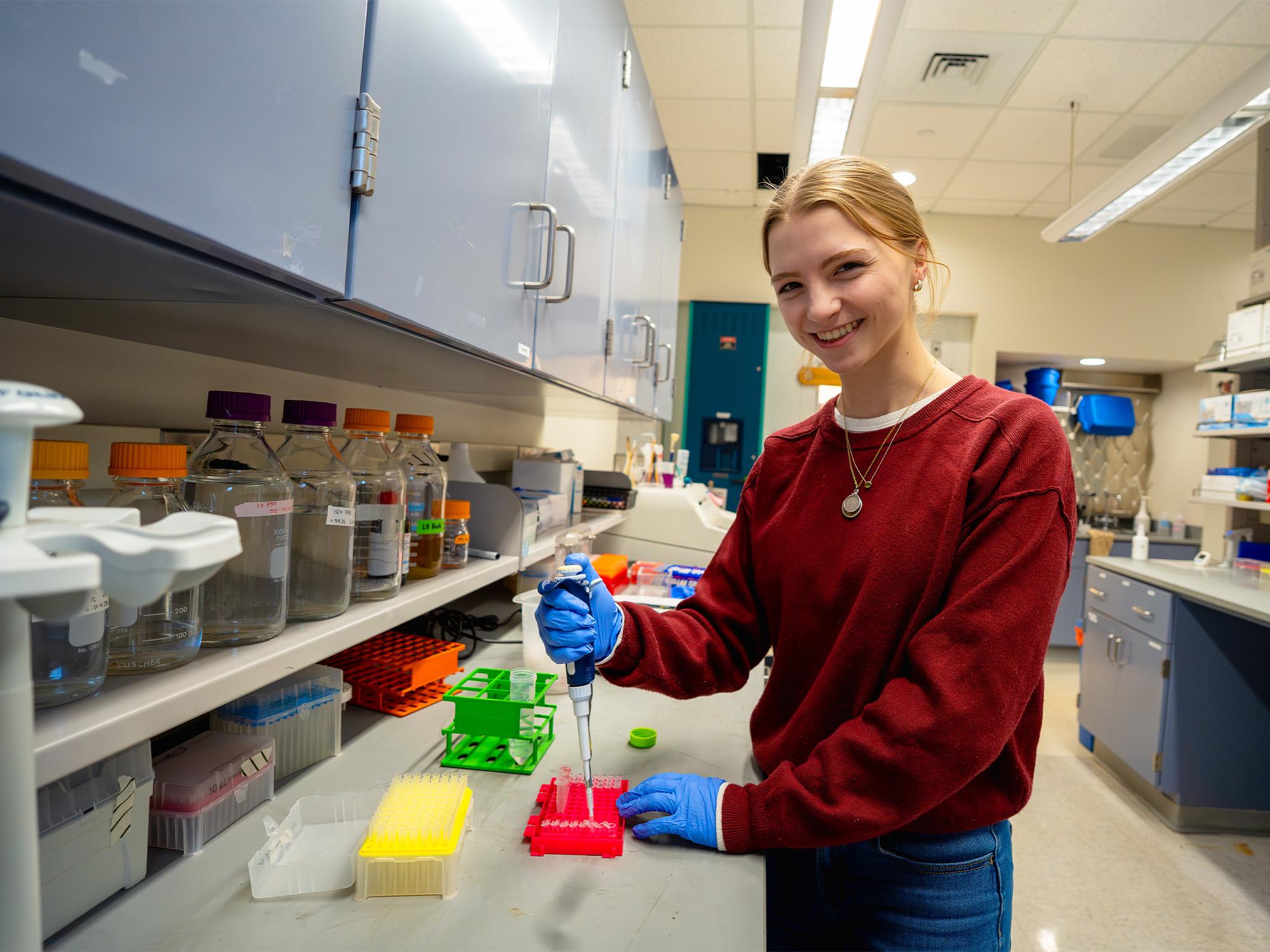 woman smiling and using a pipet in a lab