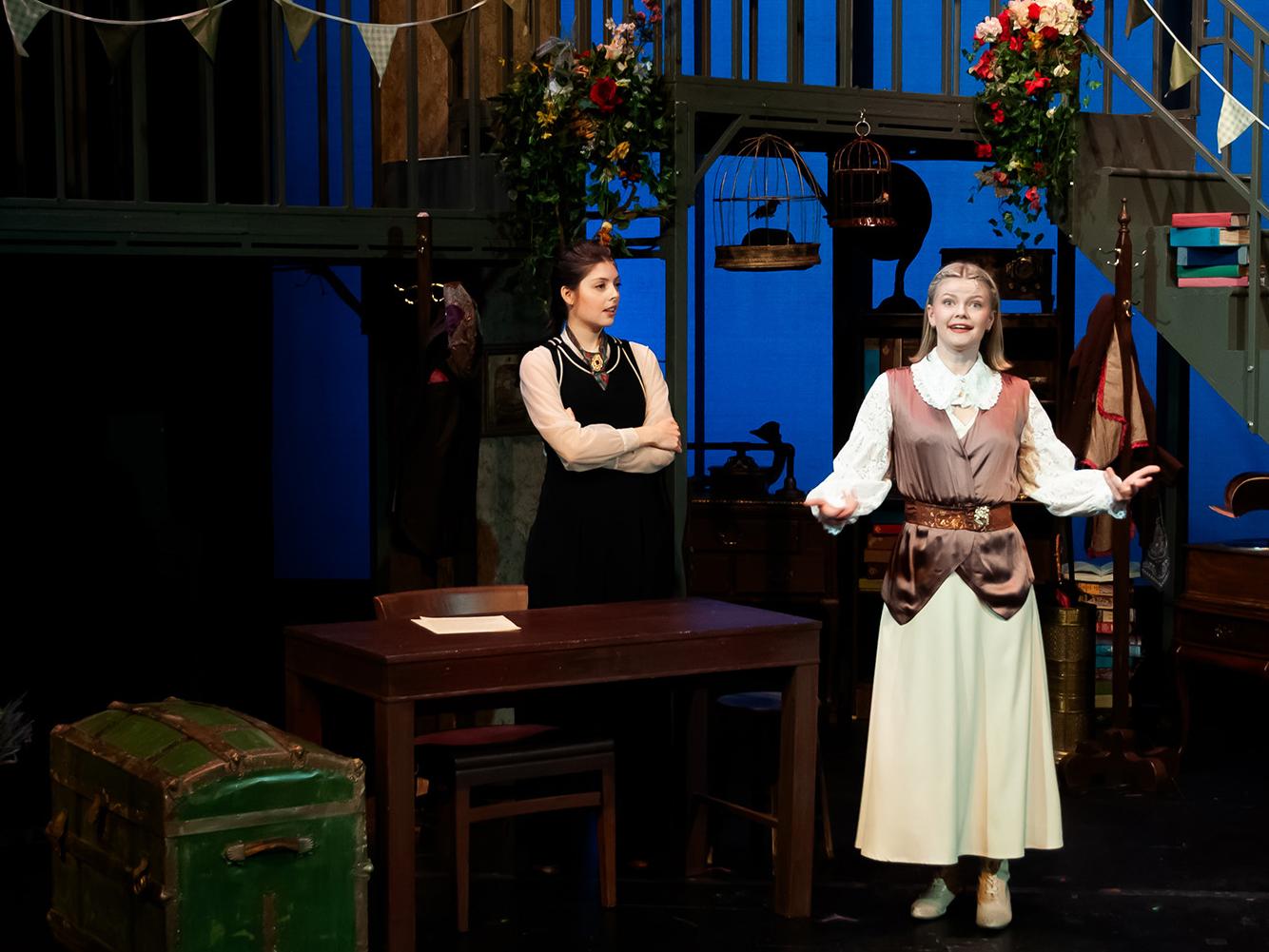 Two actors perform on a stage, one is singing