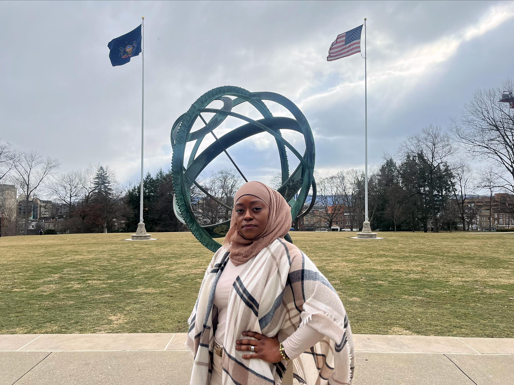 A woman poses in front of a sculpture and flag poles.