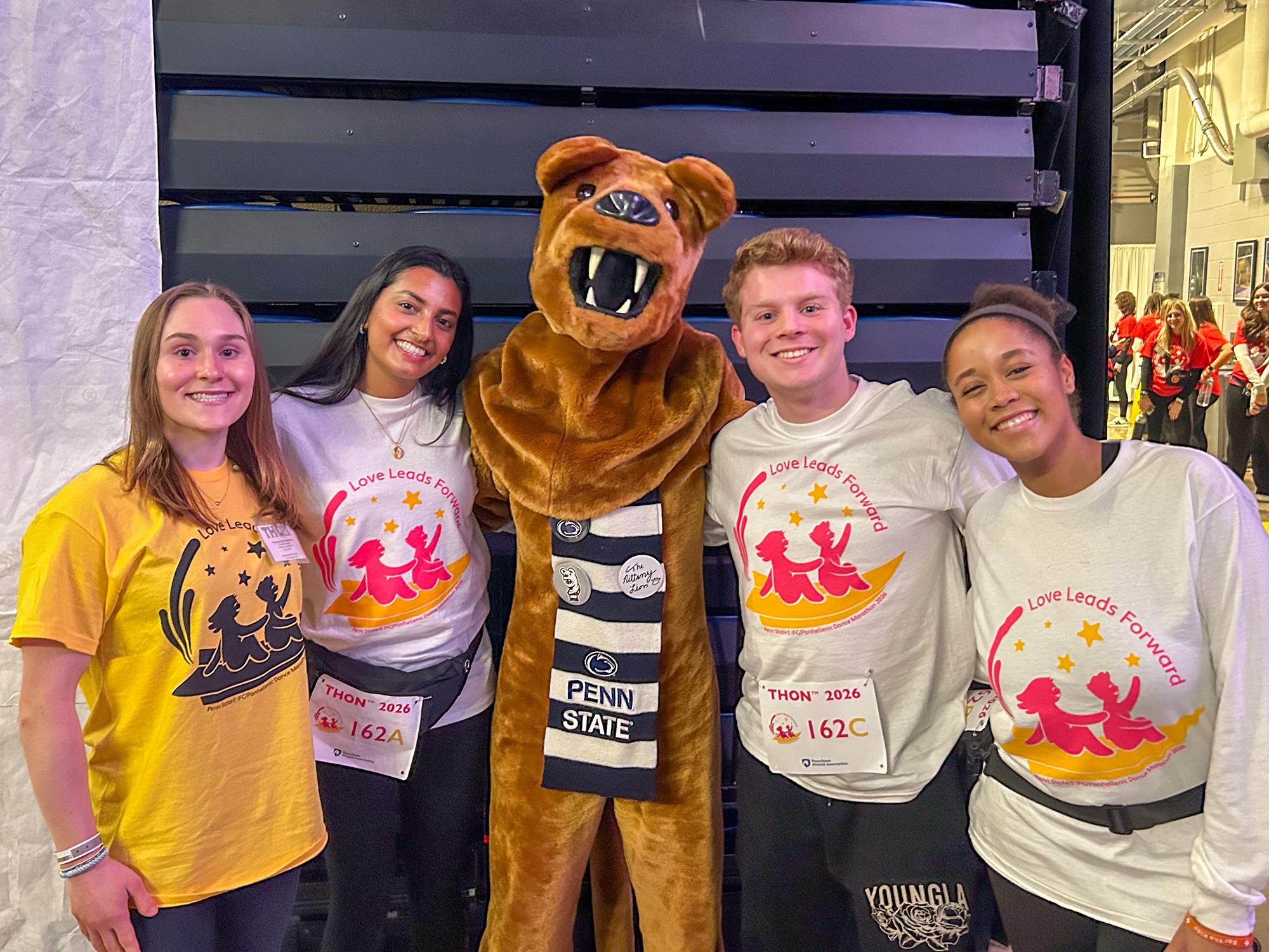 Four people pose inside the Bryce Jordan Center with the Penn State Nittany Lion mascot wearing shirts that read “Love Leads Forward.”