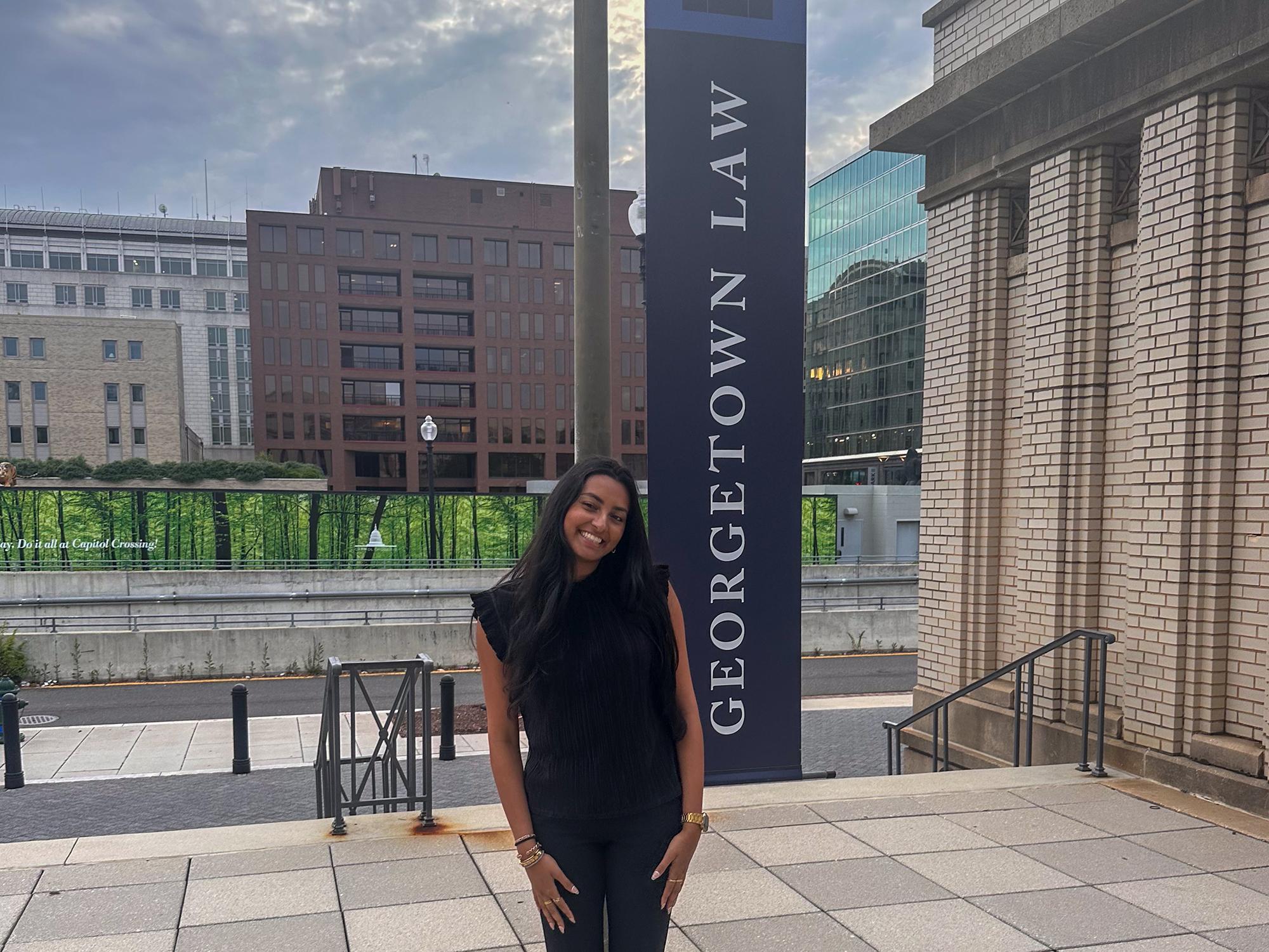 Mayuri Purani stands outside in front of a tall vertical banner that reads “Georgetown Law.”