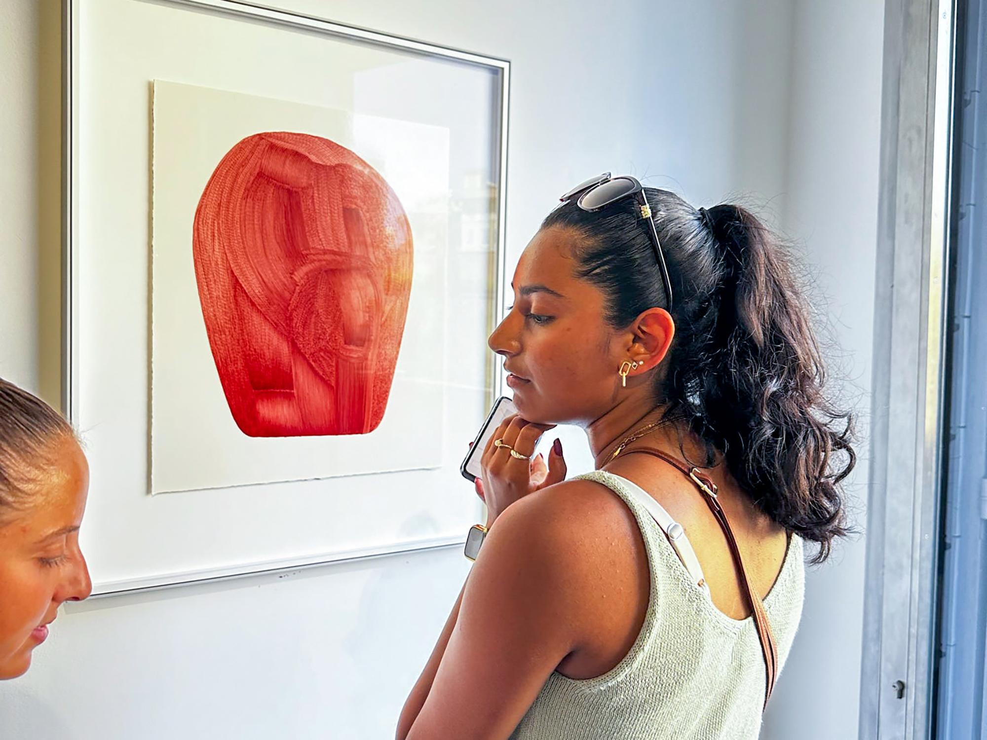 Purani looks closely at a framed abstract artwork of a large red shape on a white background.