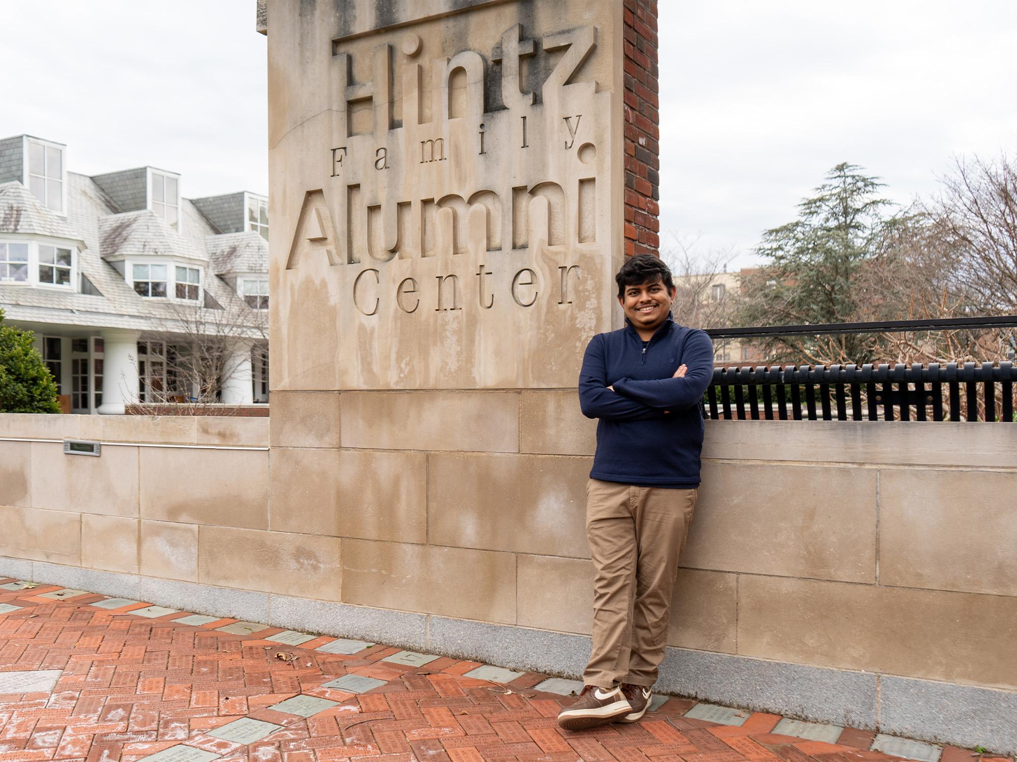 male stands next to hintz alumni center sign