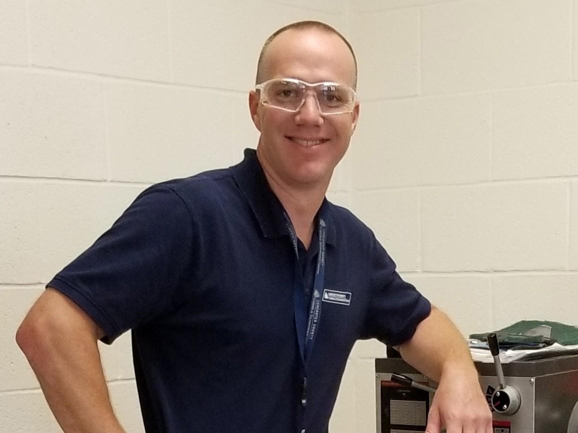A man wearing clear safety glasses and a dark blue shirt