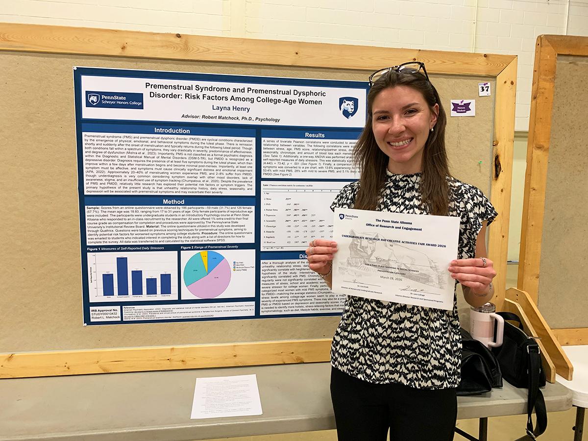 Layna Henry holds a certificate while standing in front of a research poster on premenstrual disorders at a presentation display.