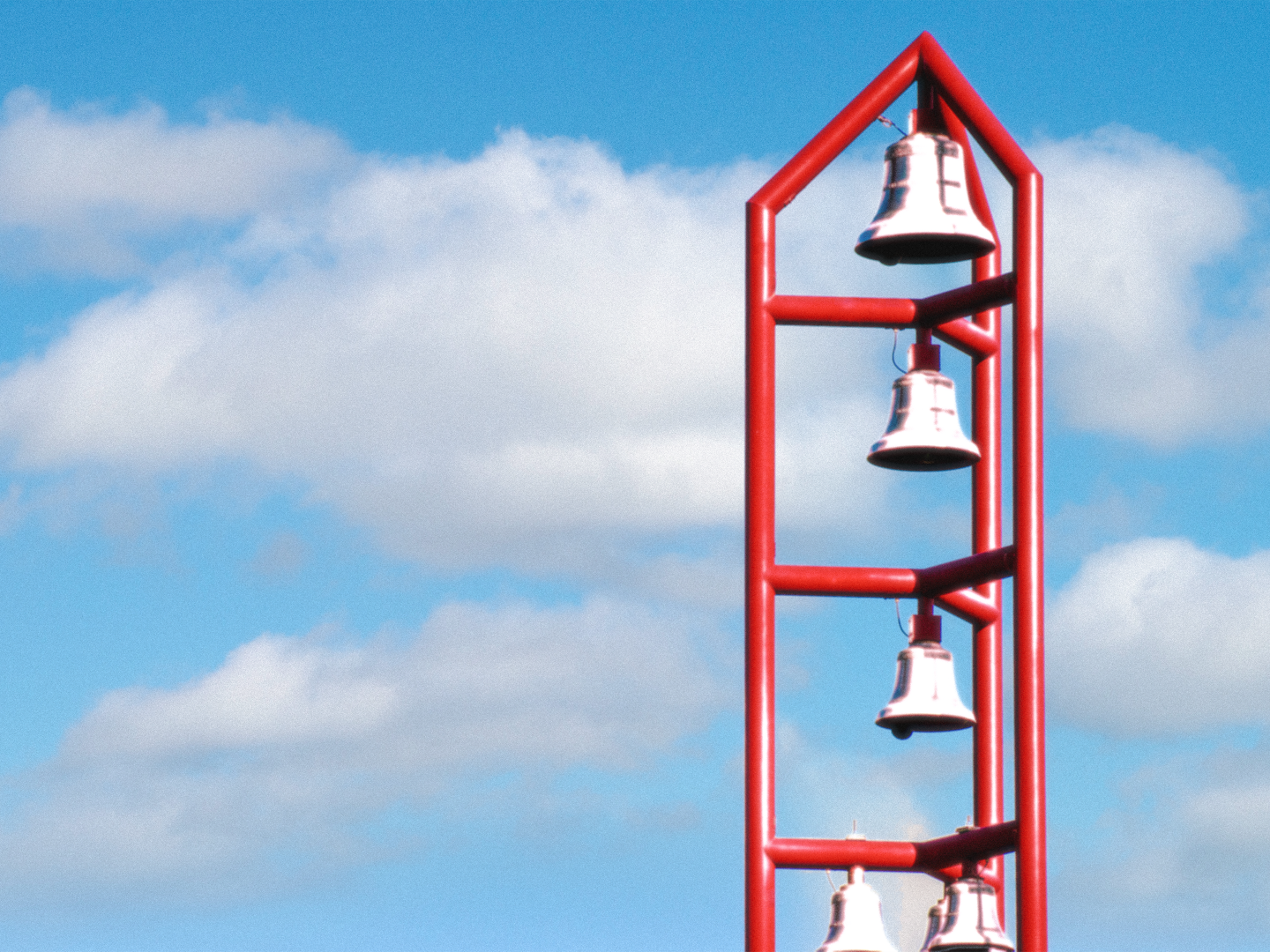 A close up picture of a red bell tower with four silver bells against a lightly cloudy blue sky