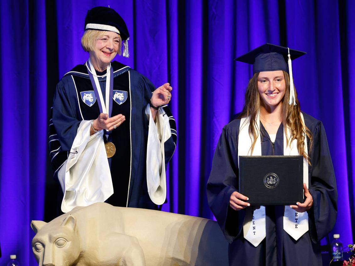 Regional Chancellor Marilyn J. Wells standing behind a nittany lion with Hope Priemon holding her diploma frame in her cap and gown. Both are smiling. 
