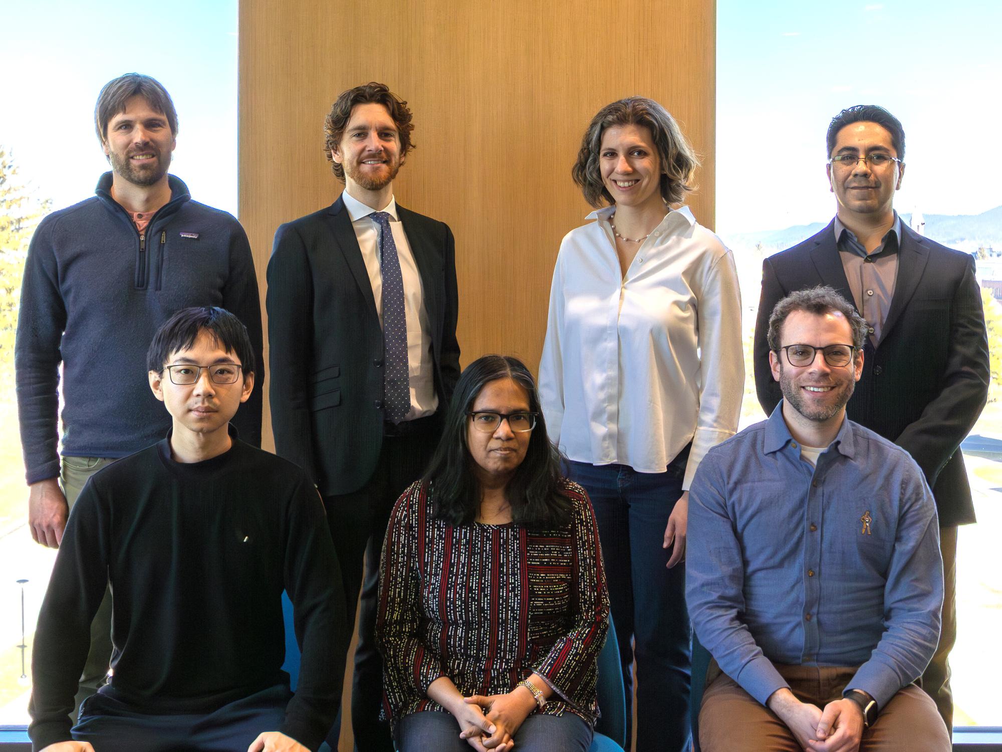 Seven of the eight early career professors standing in front of a window.
