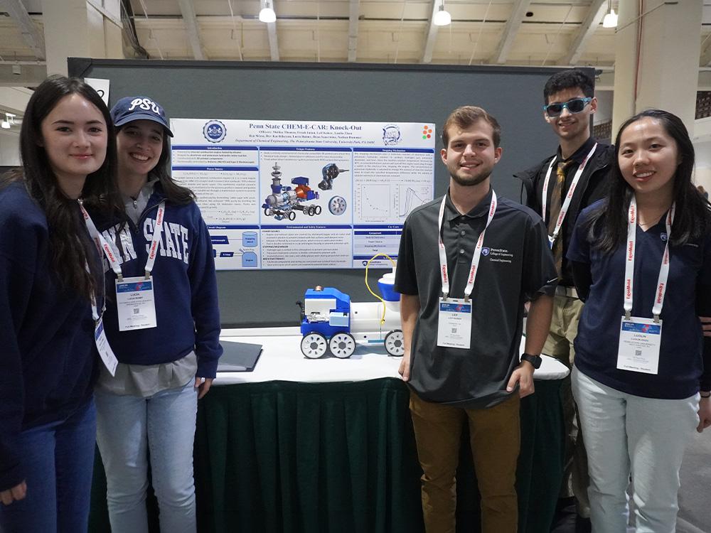 Penn State Chem-E-Car team members posing with the Knock-Out car and poster